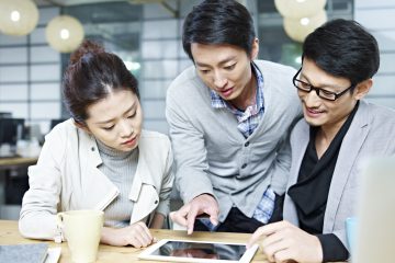 a team of young asian entrepreneurs discussing business in office using tablet computer