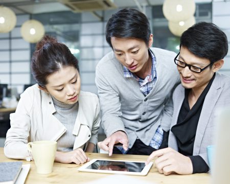 a team of young asian entrepreneurs discussing business in office using tablet computer